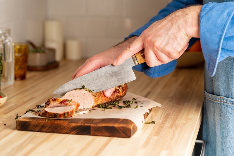 Mains d'homme tranchant un filet de porc en rondelles après cuisson.