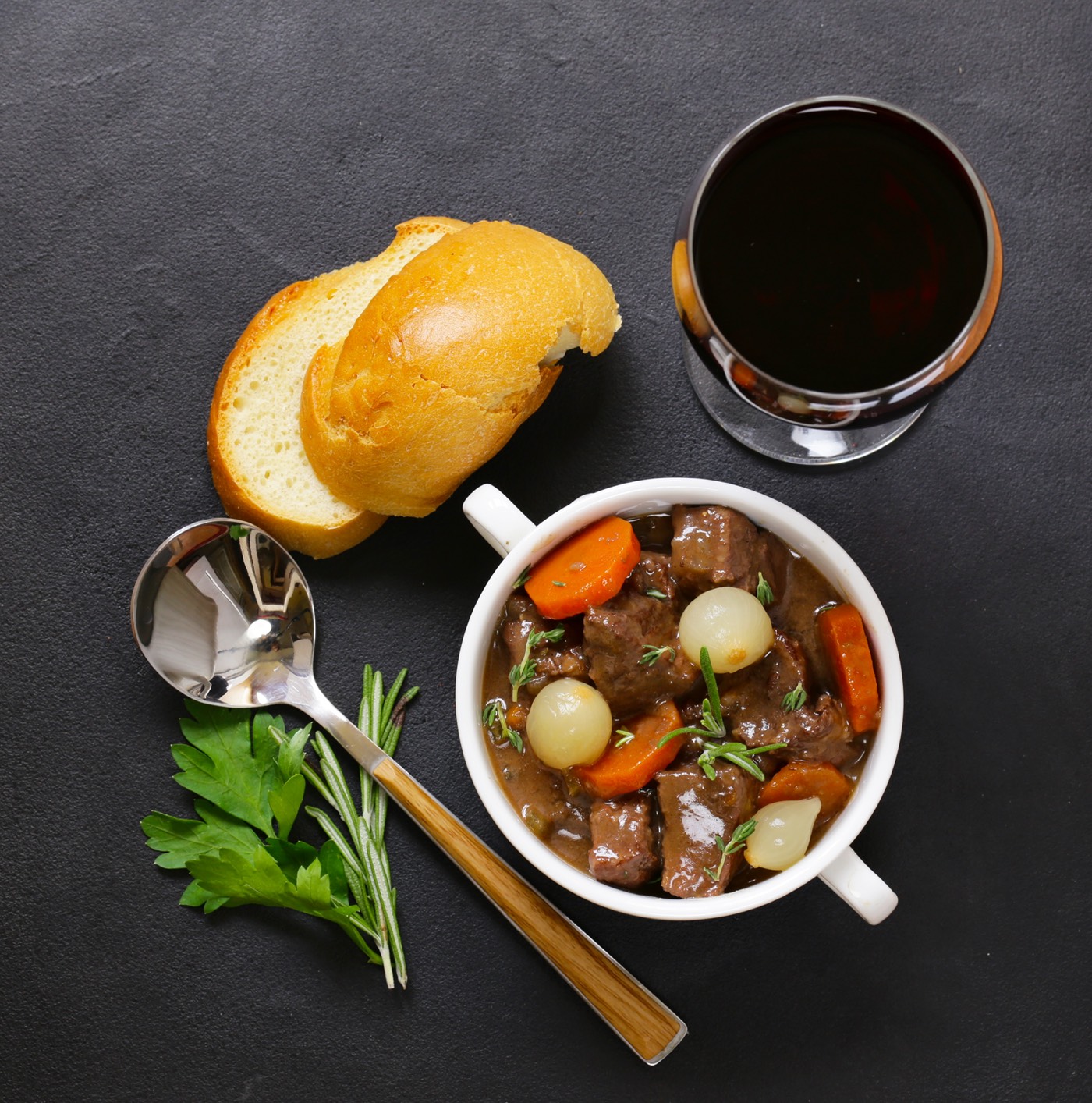 Top view of a beef stew in red wine with vegetables and herbs served on a gray table