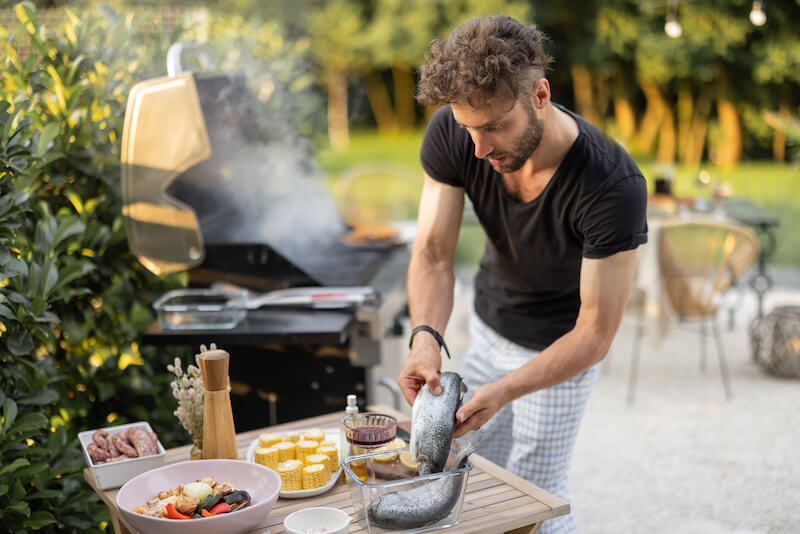 Homme cuisinant du poisson et des légumes sur un gril à l'extérieur