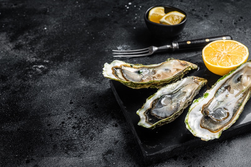 Open oysters with lemon on a black background.